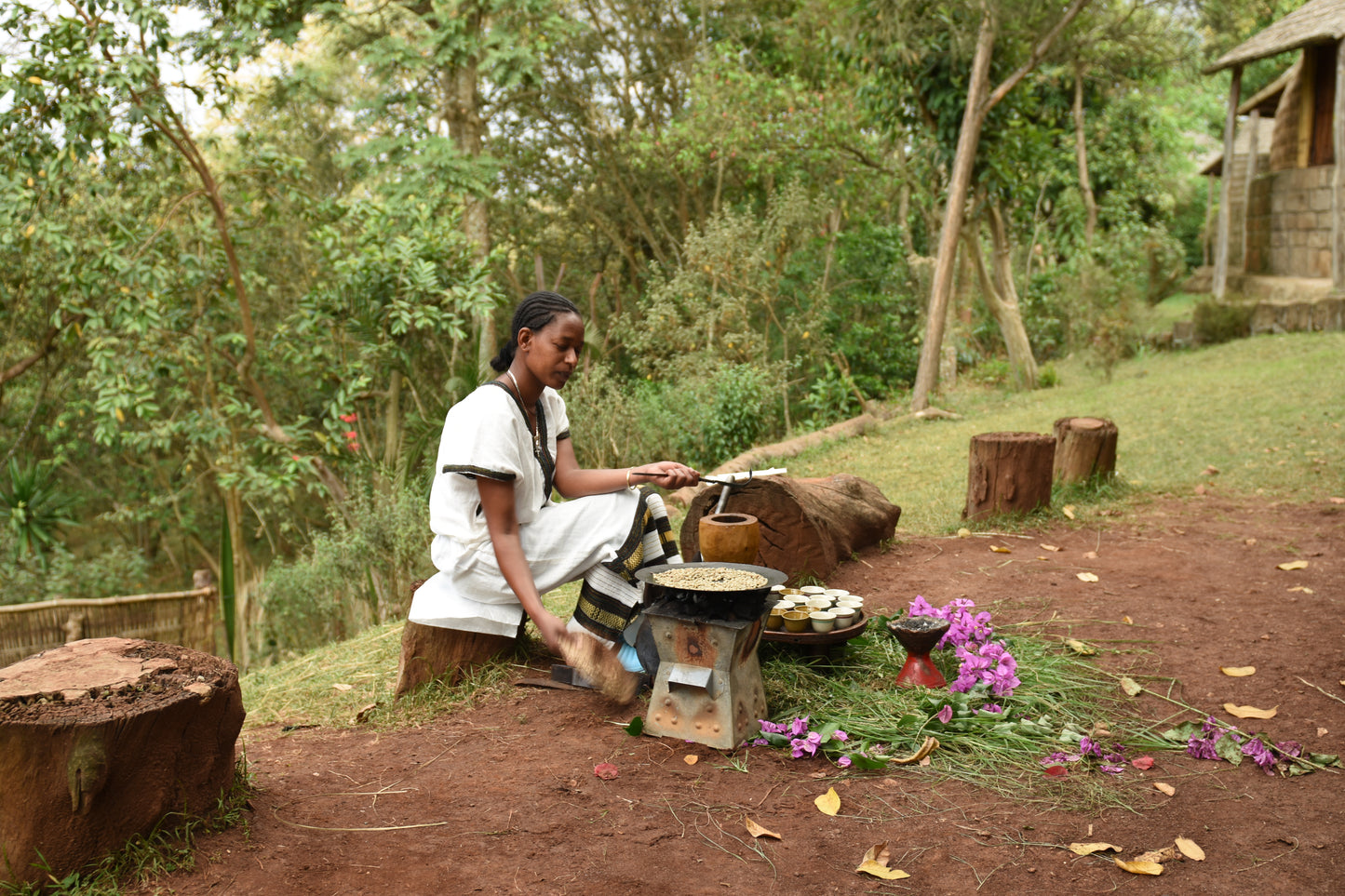 Woman preparing coffee outdoors in a natural setting with trees and stones.